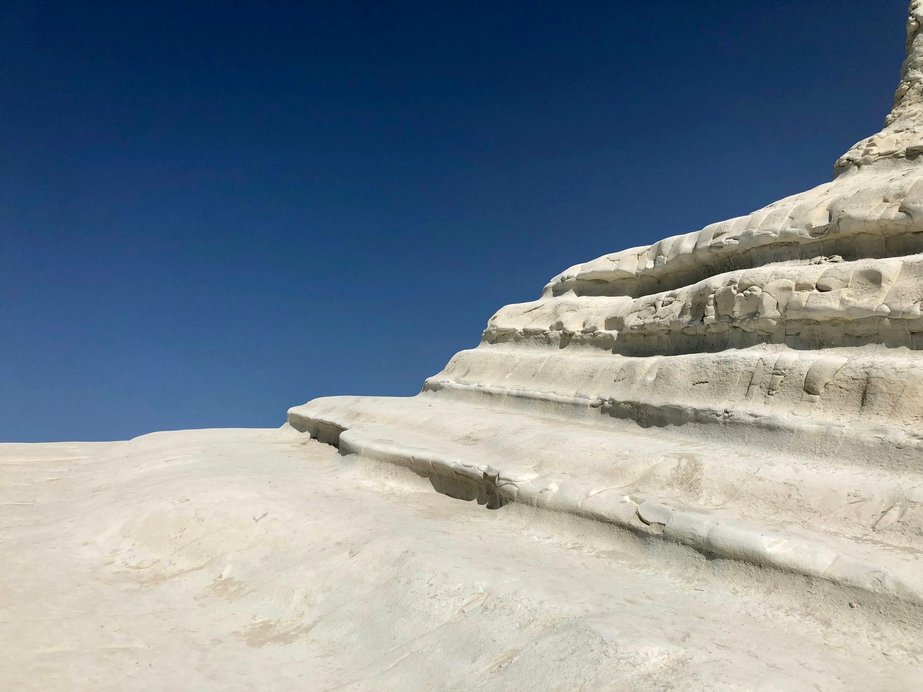 Primo piano dei gradoni di marna bianca, levigati e a strati sovrapposti, contro un cielo blu scuro senza nuvole